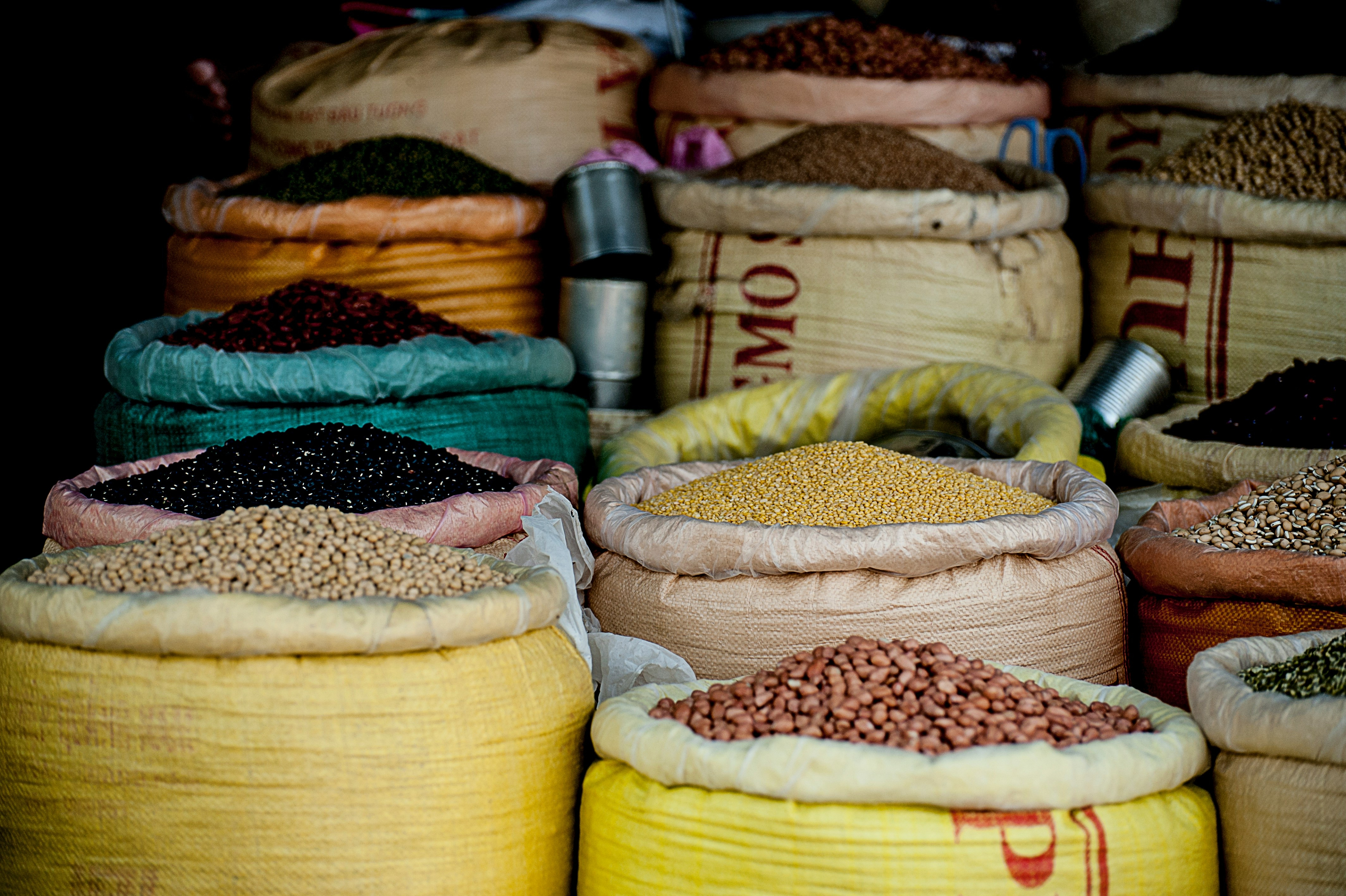 Large woven sacks filled with various colorful grains, beans, and seeds at a market.