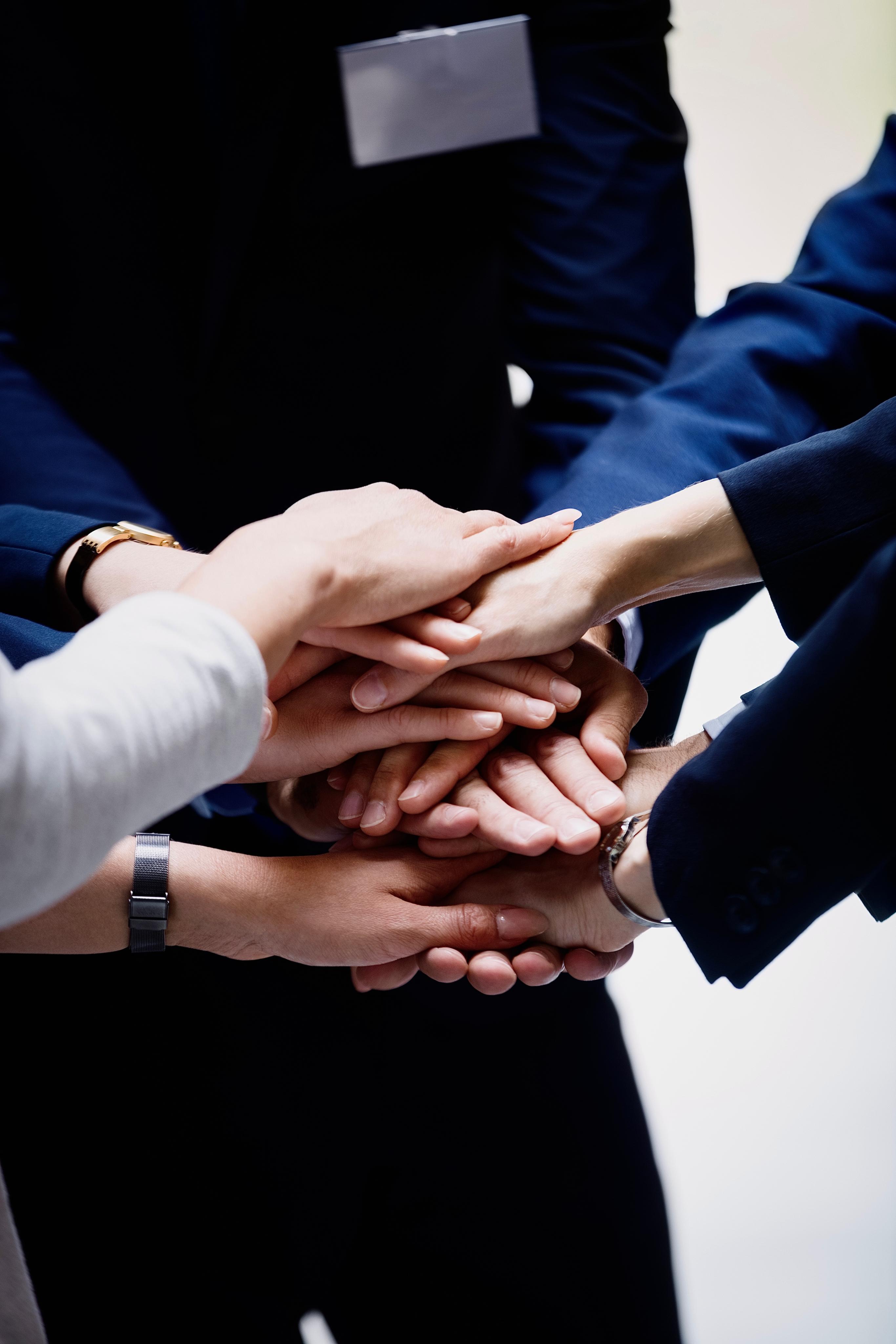 A close-up of several people in business suits stacking their hands together in the center, symbolizing teamwork and unity.